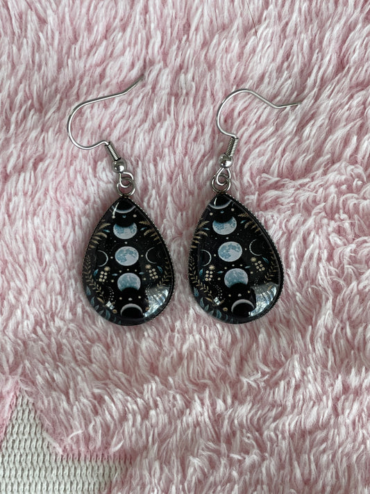 Teardrop-shaped earrings with moon phase design on a black textured background